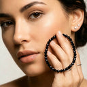 Woman holding a black tourmaline beaded bracelet to her face against a neutral background