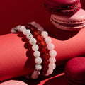 Stack of beaded bracelets on a red surface with pink macarons