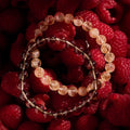 Two beaded bracelets on a bed of raspberries with a red background