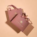Two pink 'Awaken' bags with ribbons on a beige background