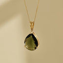 Gold necklace with a teardrop-shaped green gemstone pendant on a beige background moldavite 
