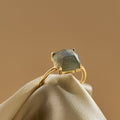 Gold ring with a green  and blue labradorite gemstone on beige fabric against a brown background