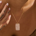 Gold rose quartz necklace with a rectangular pendant on a person wearing a brown top.