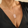Woman wearing a black outfit with sheer sleeves against a beige background wearing a rose quartz crystal necklace
