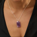 Woman wearing a black top and an amethyst necklace with a purple pendant against a beige background