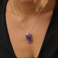 Woman wearing a black top and an amethyst necklace with a purple pendant against a beige background