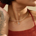 Woman with short hair wearing a red top and silver snake choker chain necklace against a beige background