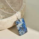 Necklace with a blue lapis lazuli and white stone pendant on a neutral background