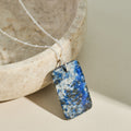 Necklace with a blue lapis lazuli and white stone pendant on a neutral background