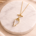 Gold necklace with a moonstone triangular pendant on a marble surface